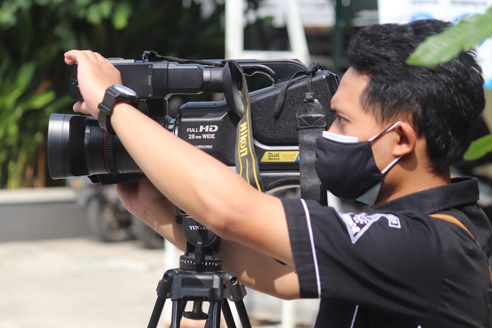 Hombre en camiseta blanca y negra sosteniendo una cámara DSLR negra