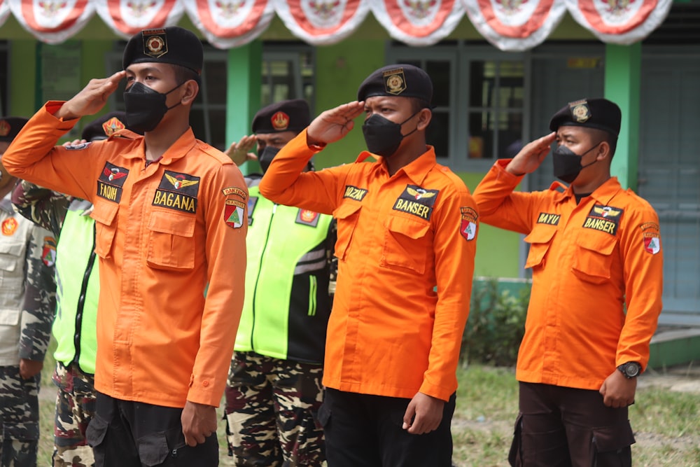 man in orange button up shirt standing beside man in black and white fitted cap