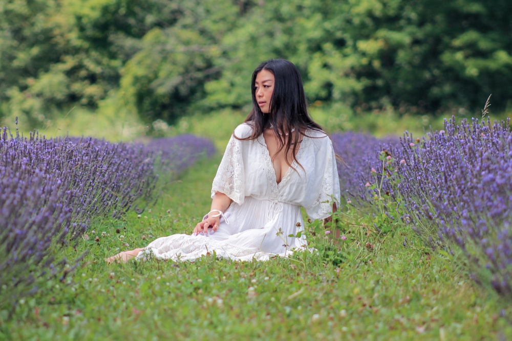 femme en robe blanche assise sur le champ d’herbe verte pendant la journée