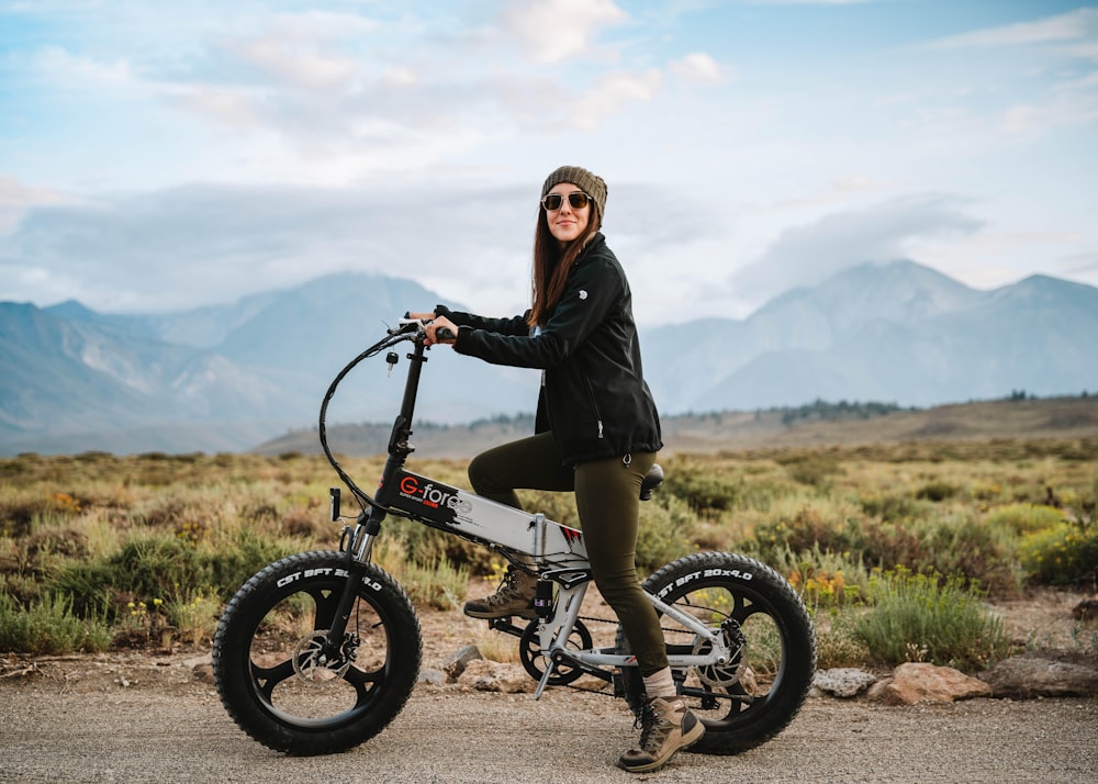 woman in black jacket riding on red bicycle on green grass field during daytime