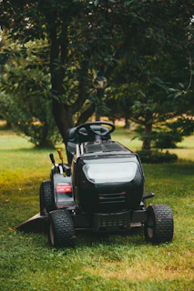 A black ride‑on lawn mower sitting on a green grass field during daytime, ready for professional law