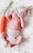 A baby wearing knitted accessories, including a hat and diaper cover, is peacefully lying on a soft, white blanket. Beside the baby is a plush, knitted carrot.