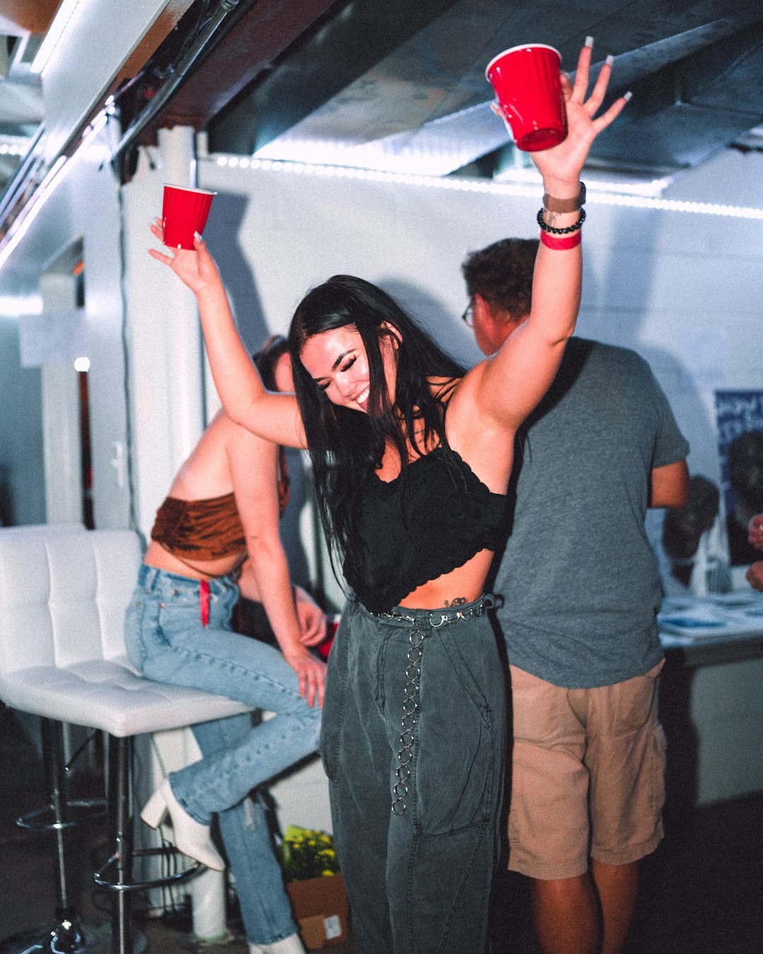 woman in black tank top and blue denim jeans holding red plastic bottle