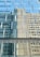 Reflective glass windows of a modern building capturing the distorted reflection of an adjacent structure with rectangular and square patterns. The windows create a geometric visual effect with its repetitive design.