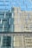 Reflective glass windows of a modern building capturing the distorted reflection of an adjacent structure with rectangular and square patterns. The windows create a geometric visual effect with its repetitive design.