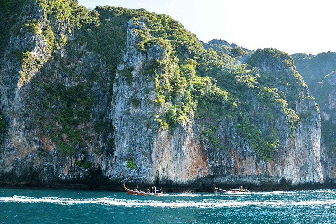 brown boat on sea near green and brown rock formation during daytime