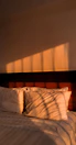 Sunlight filtering through large windows onto a comfortable bed with earth-toned bedding.