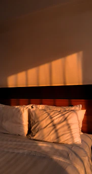 Sunlight filters through linen curtains onto soft sandy-toned pillows by an ocean-view window.