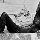 grayscale photo of man in jacket and pants sitting on ground
