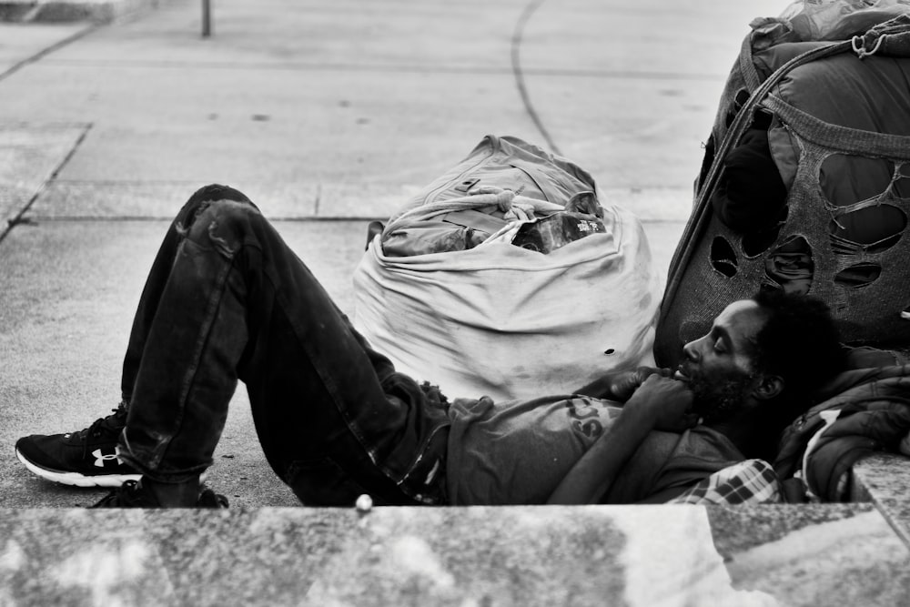 grayscale photo of man in jacket and pants sitting on ground