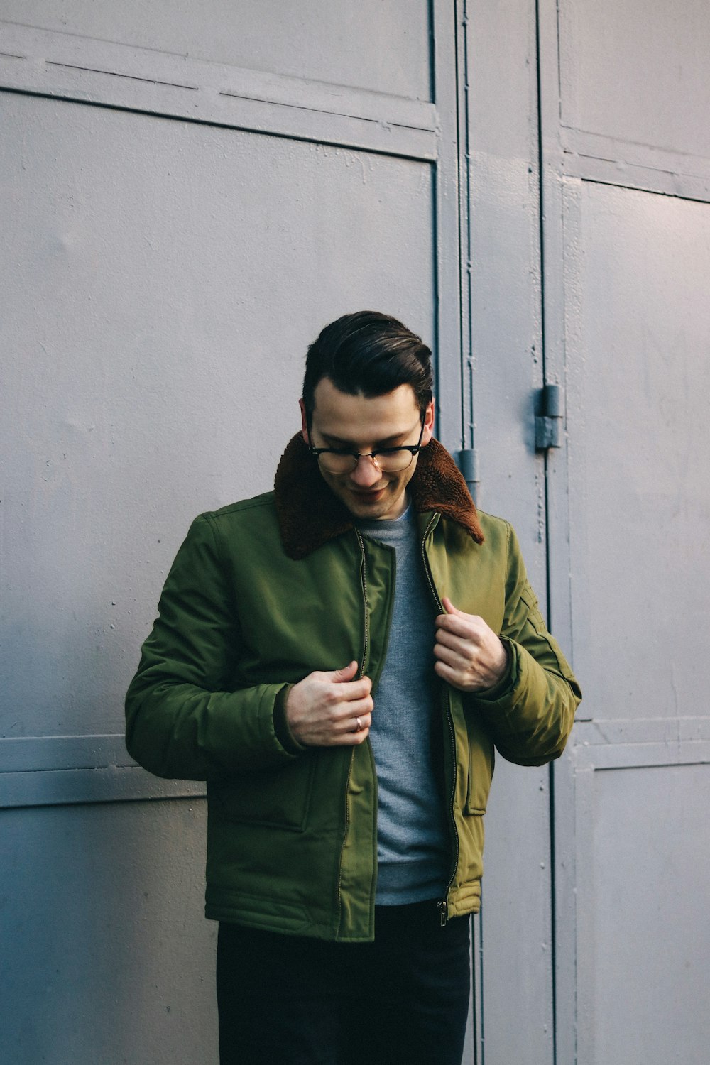 man in green jacket standing near white wall