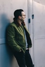 man in green dress shirt standing beside blue wall