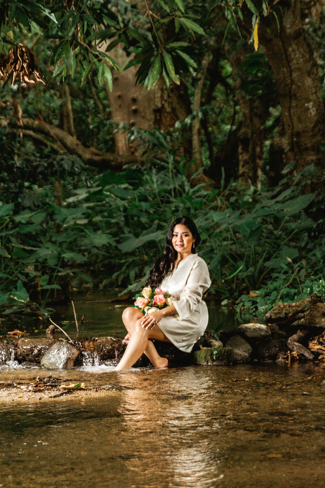 woman in white robe sitting on rock in river