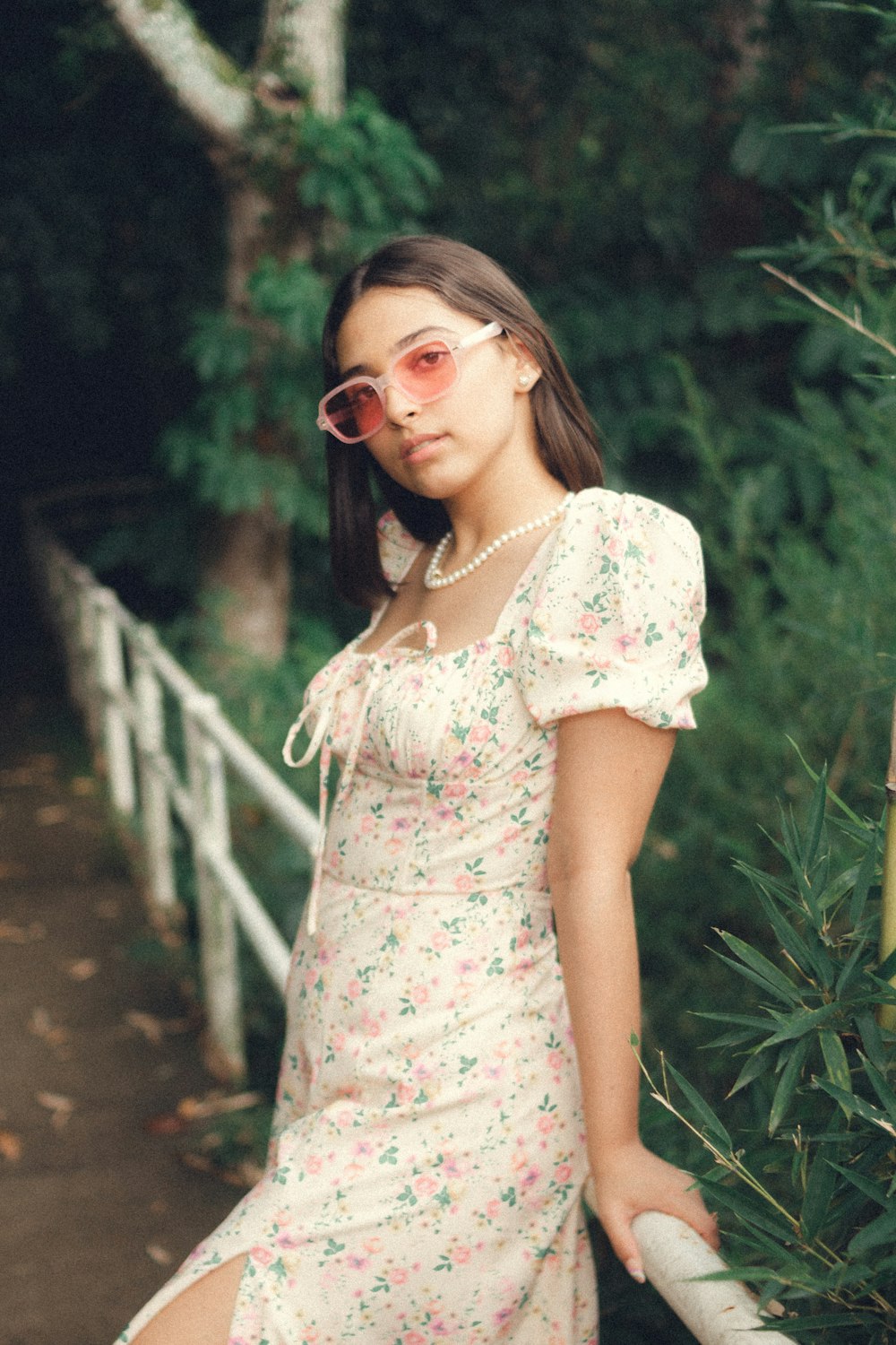 woman in white floral dress wearing sunglasses standing on wooden bridge