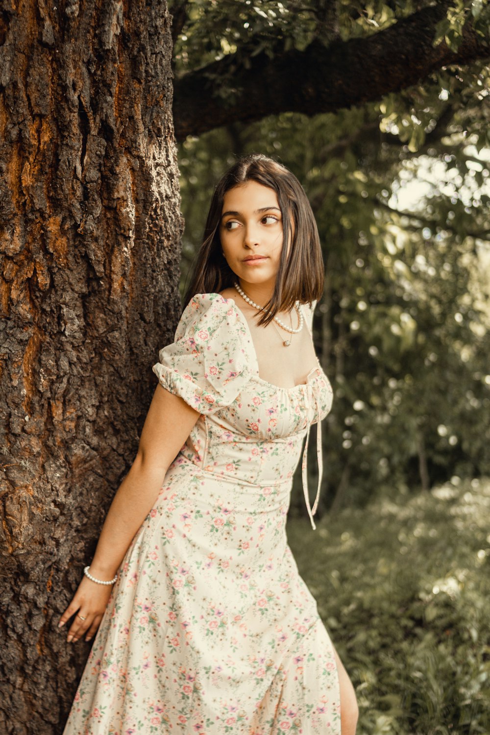 woman in white and pink floral dress standing beside brown tree