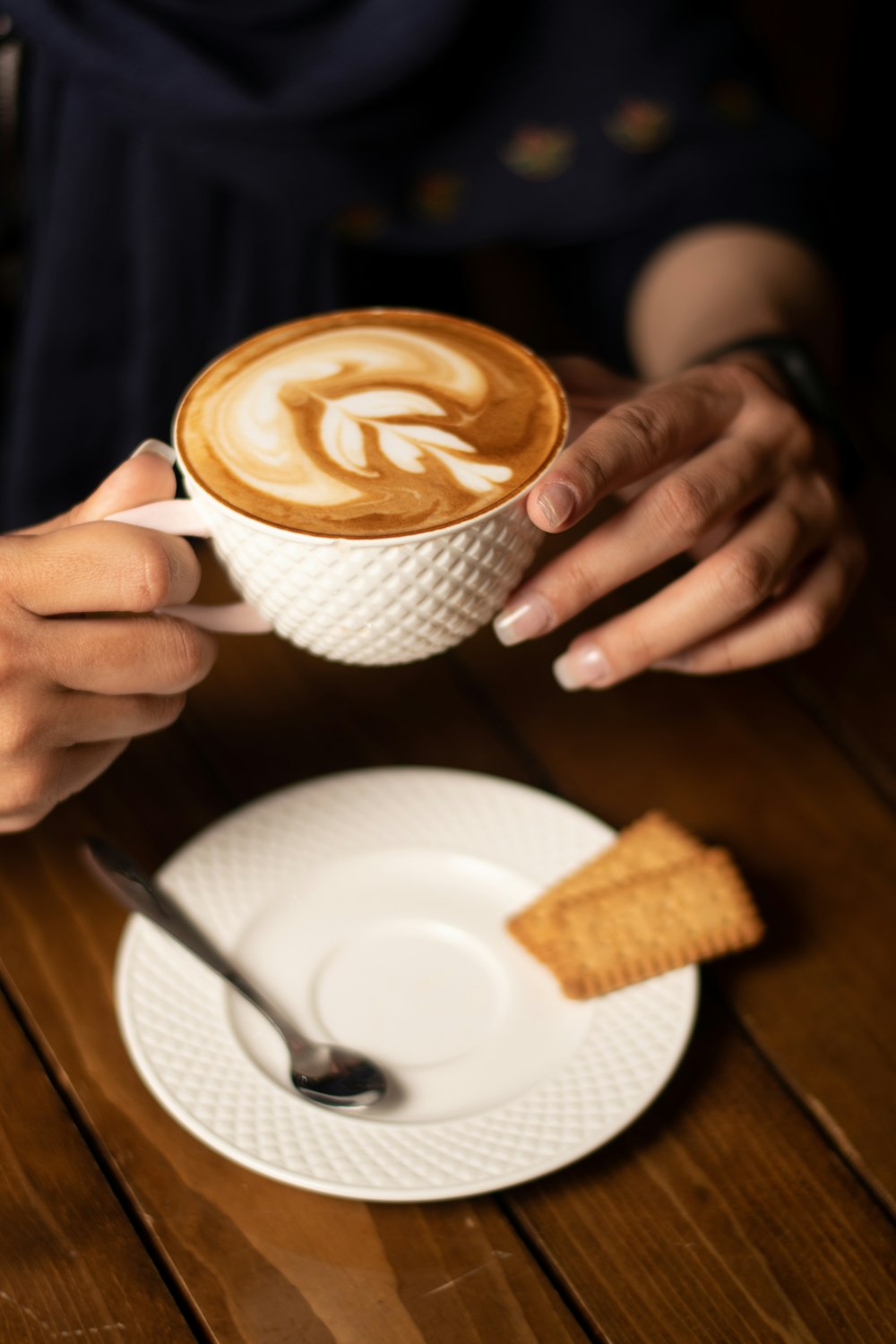 Person mit weißem Keramikbecher mit Cappuccino