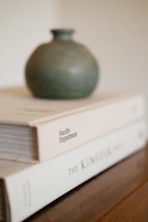 Close-up of a textured ceramic vase sitting on a sleek marble tabletop beside a small stack of design books.