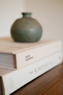 Close-up of a textured ceramic vase sitting on a sleek marble tabletop beside a small stack of design books.