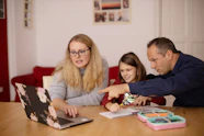 A woman and a man helping a child with schoolwork on a laptop