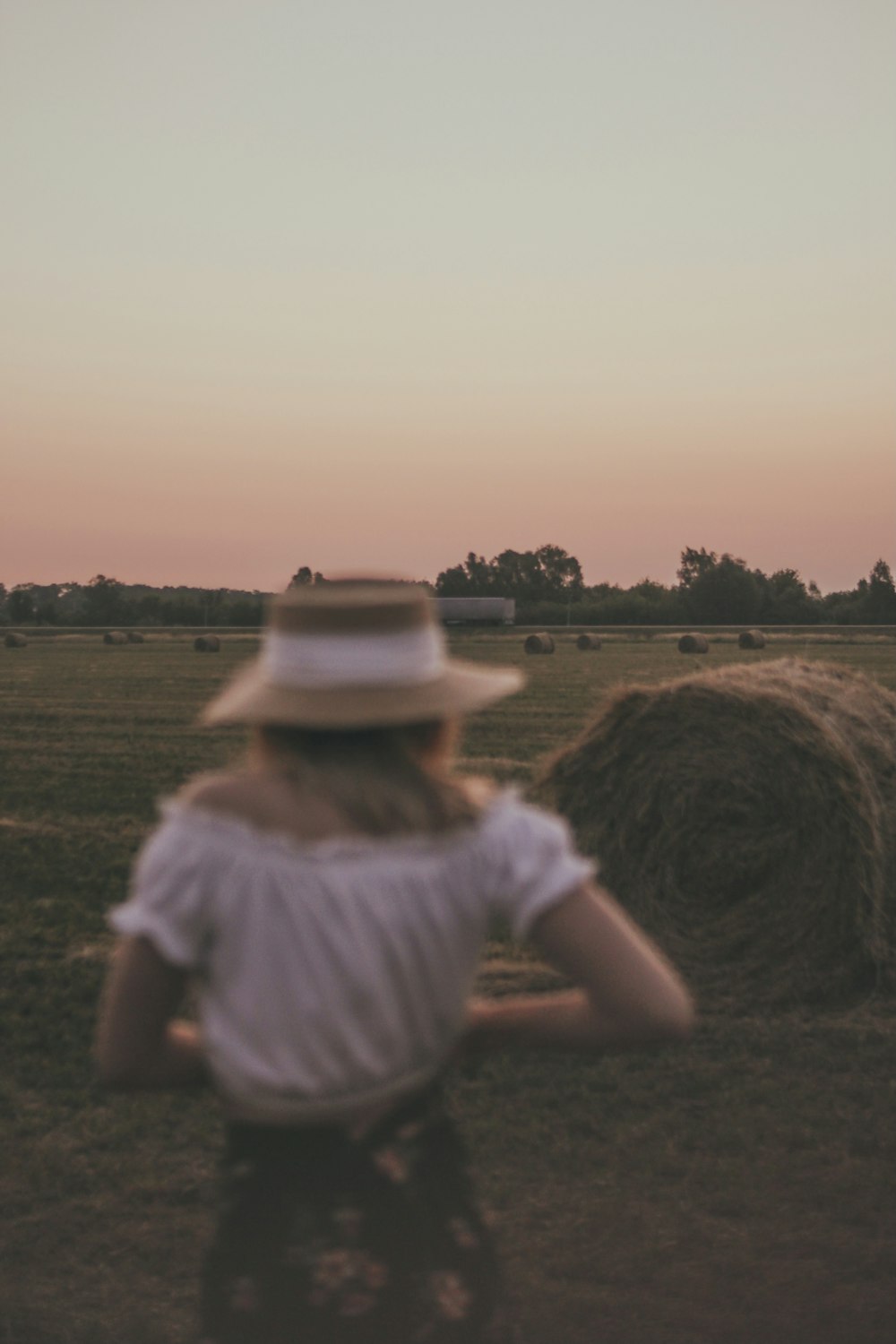 woman in white shirt and brown hat sitting on brown grass field during daytime