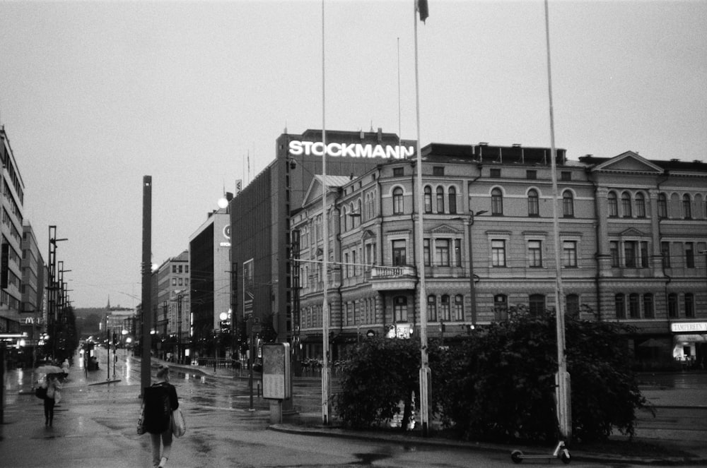 grayscale photo of people walking on sidewalk near building