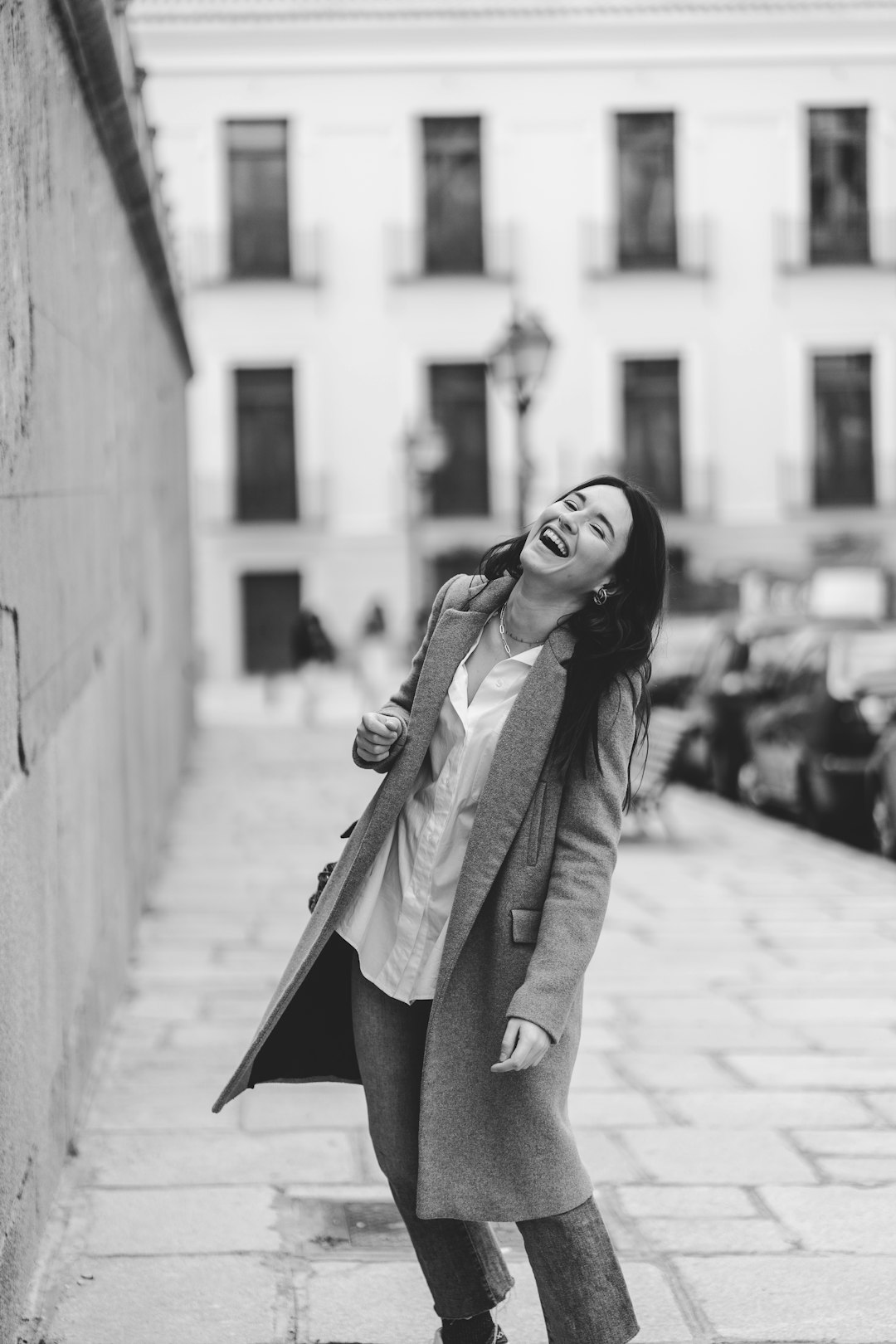 woman in coat and pants standing on sidewalk in grayscale photography