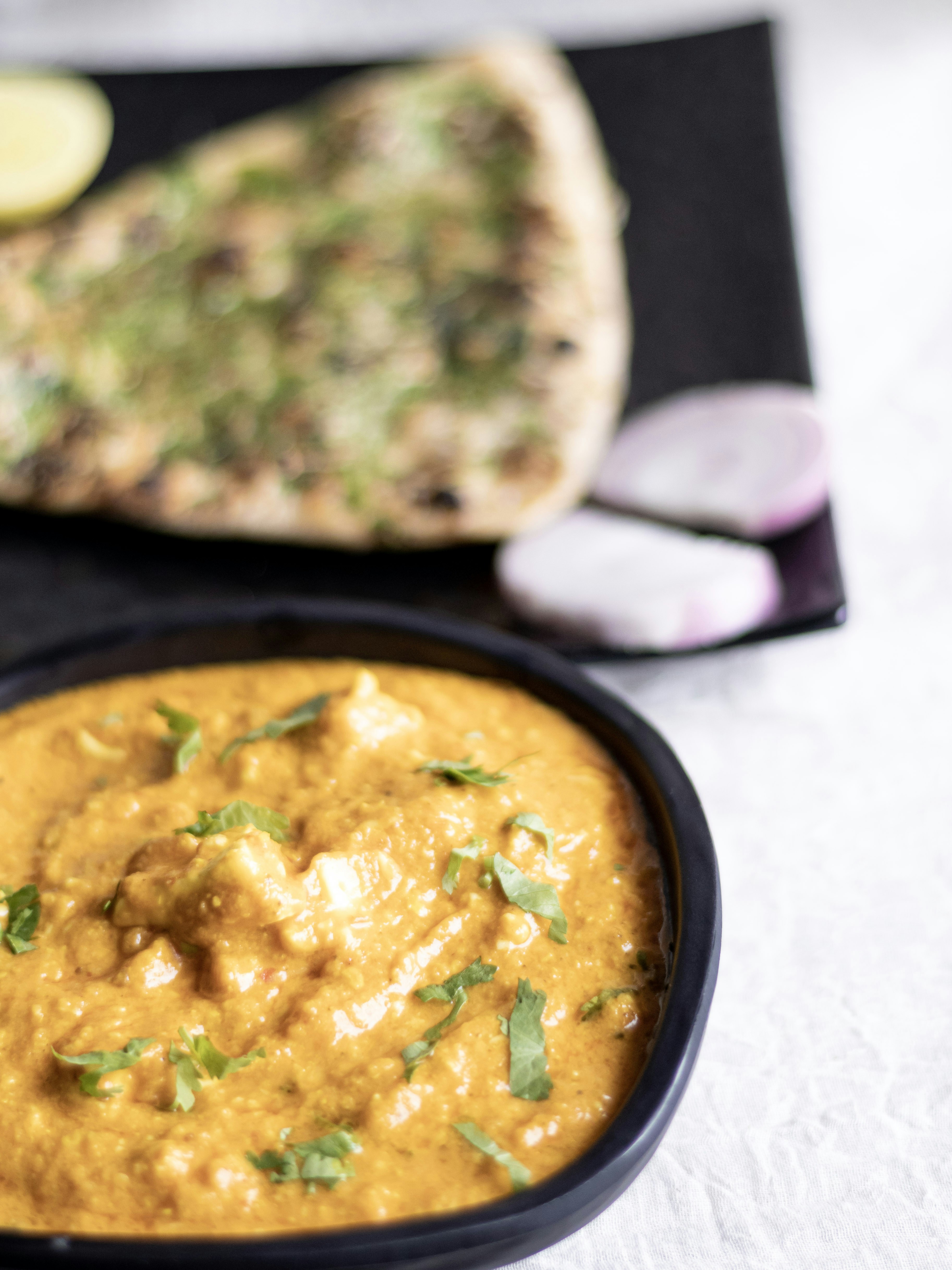 Rich orange butter chicken curry in a bowl with naan bread