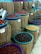 Multiple burlap sacks filled with various types of beans and grains are displayed. Each sack has a colored bowl on top with a scoop inside, and price tags are visible. The sacks are arranged in neat rows, showcasing a variety of colors and textures.