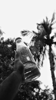 Hands holding a glass bottle of wood pressed oil with olive branches in the background.