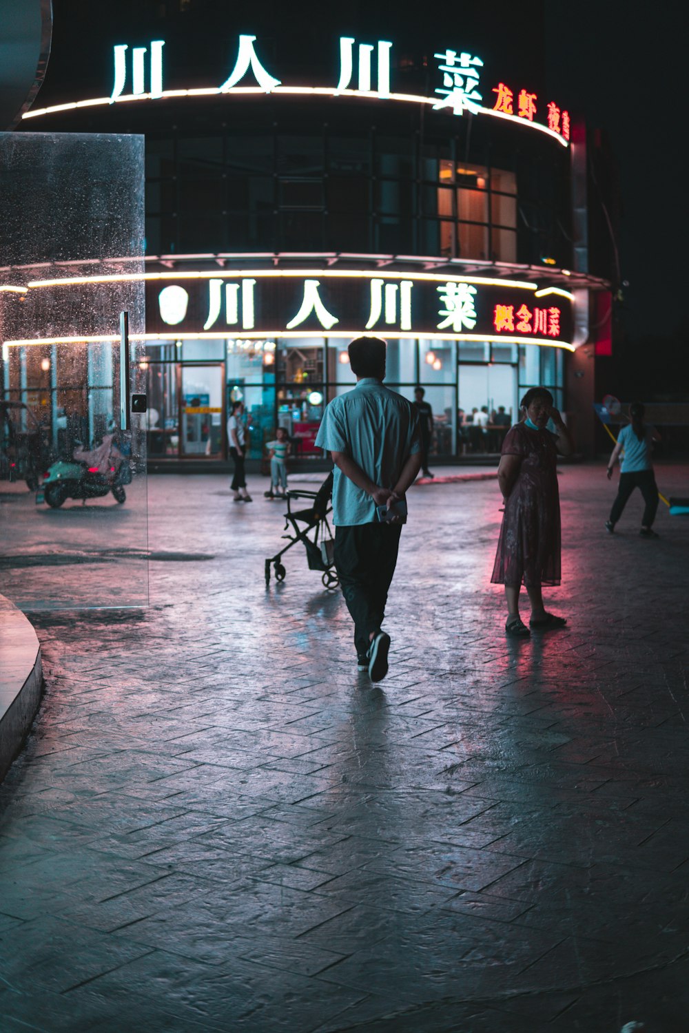 man in black jacket and black pants walking with black dog on sidewalk during night time