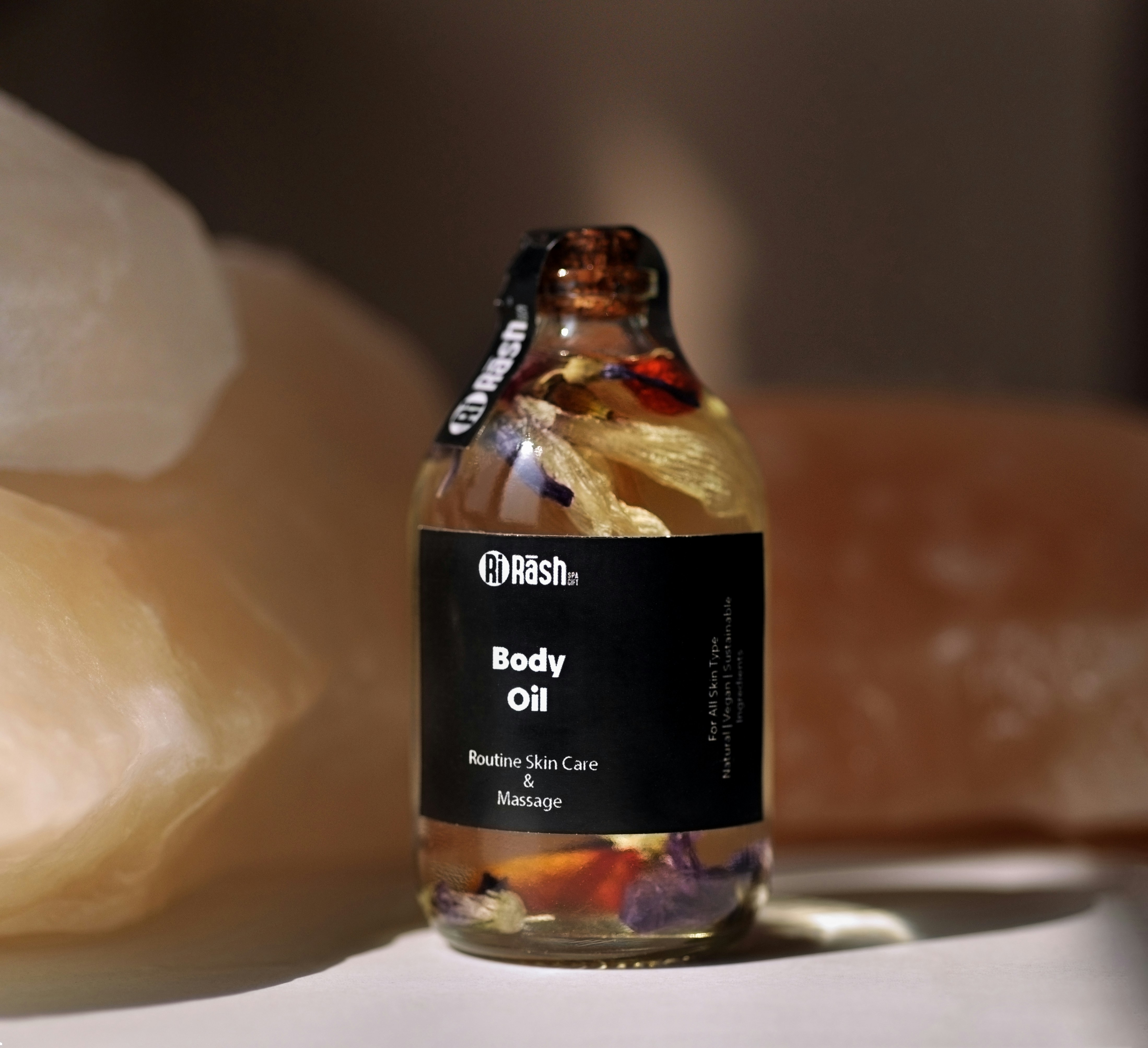 Amber glass bottle of body oil surrounded by botanical ingredients on wooden surface