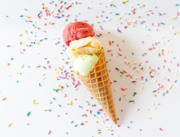 A colorful display of assorted ice cream scoops in waffle cones with fresh fruit garnishes.