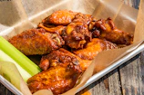 A vibrant platter of medium-sized wings covered in spicy BBQ sauce with fresh herbs.
