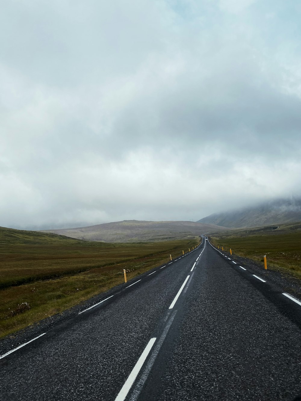 route goudronnée grise entre un champ d’herbe verte sous un ciel nuageux gris pendant la journée