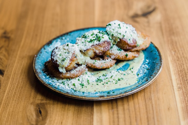 A plate of delicious fried food garnished with grated cheese and chopped herbs on a rustic wooden table. The dish appears to be served with a creamy sauce, adding a gourmet touch to the presentation.