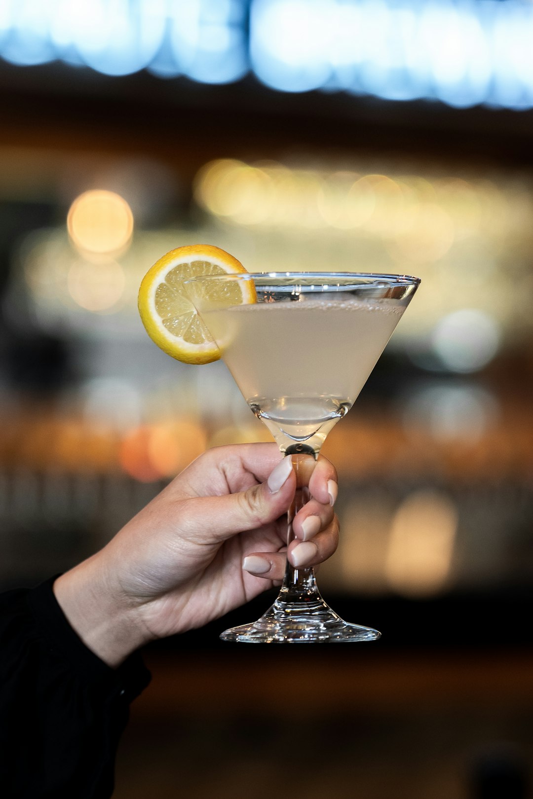 person holding clear cocktail glass with sliced lemon