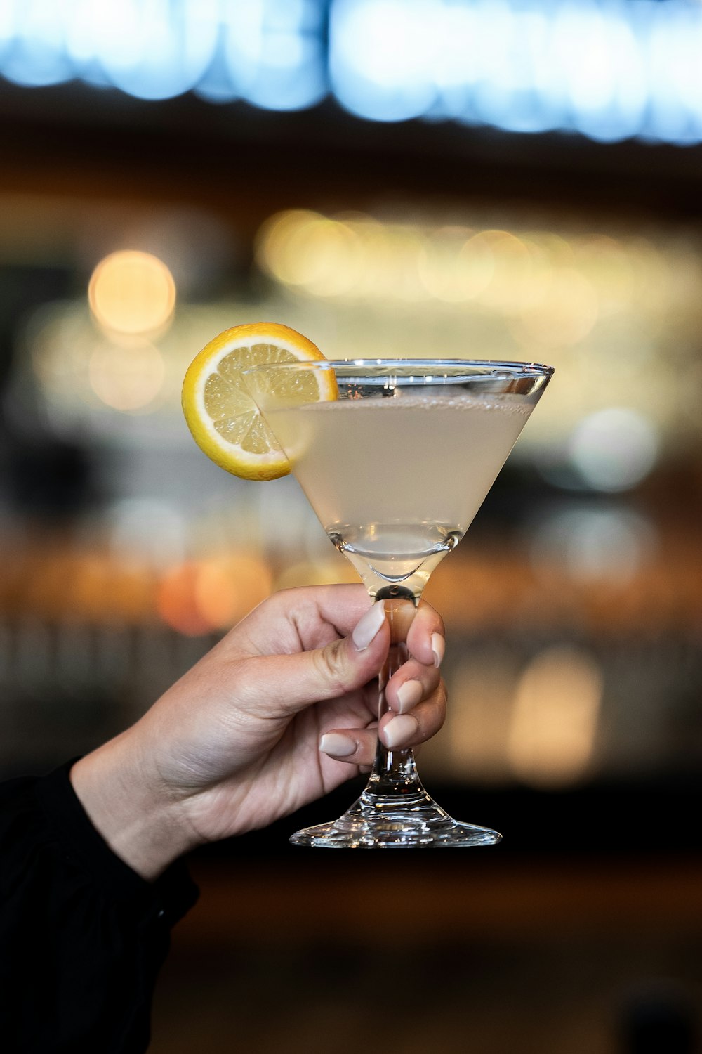 person holding clear cocktail glass with sliced lemon