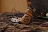 Two handcrafted necklaces are displayed on a textured wooden surface. The first pendant resembles a polished stone wrapped in copper wire, while the second one is a metallic disk adorned with red gems. A string of amber-like beads accompanies the first pendant, adding to the earthy aesthetic.