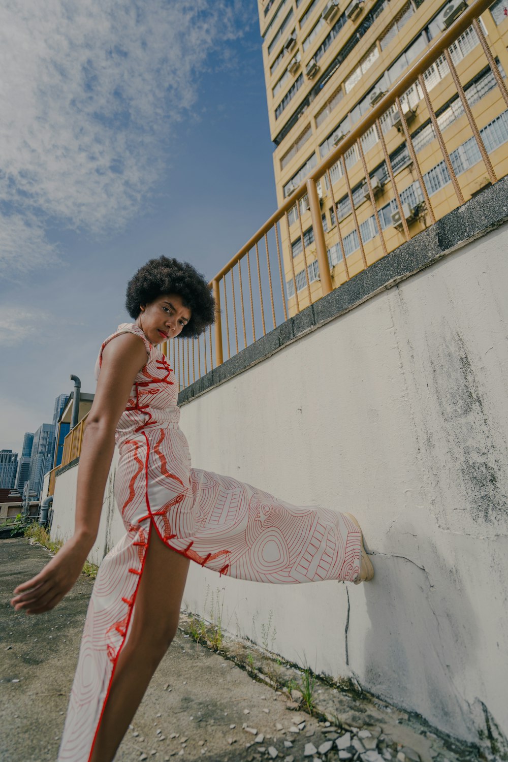 woman in white and red floral sleeveless dress standing beside white concrete building during daytime