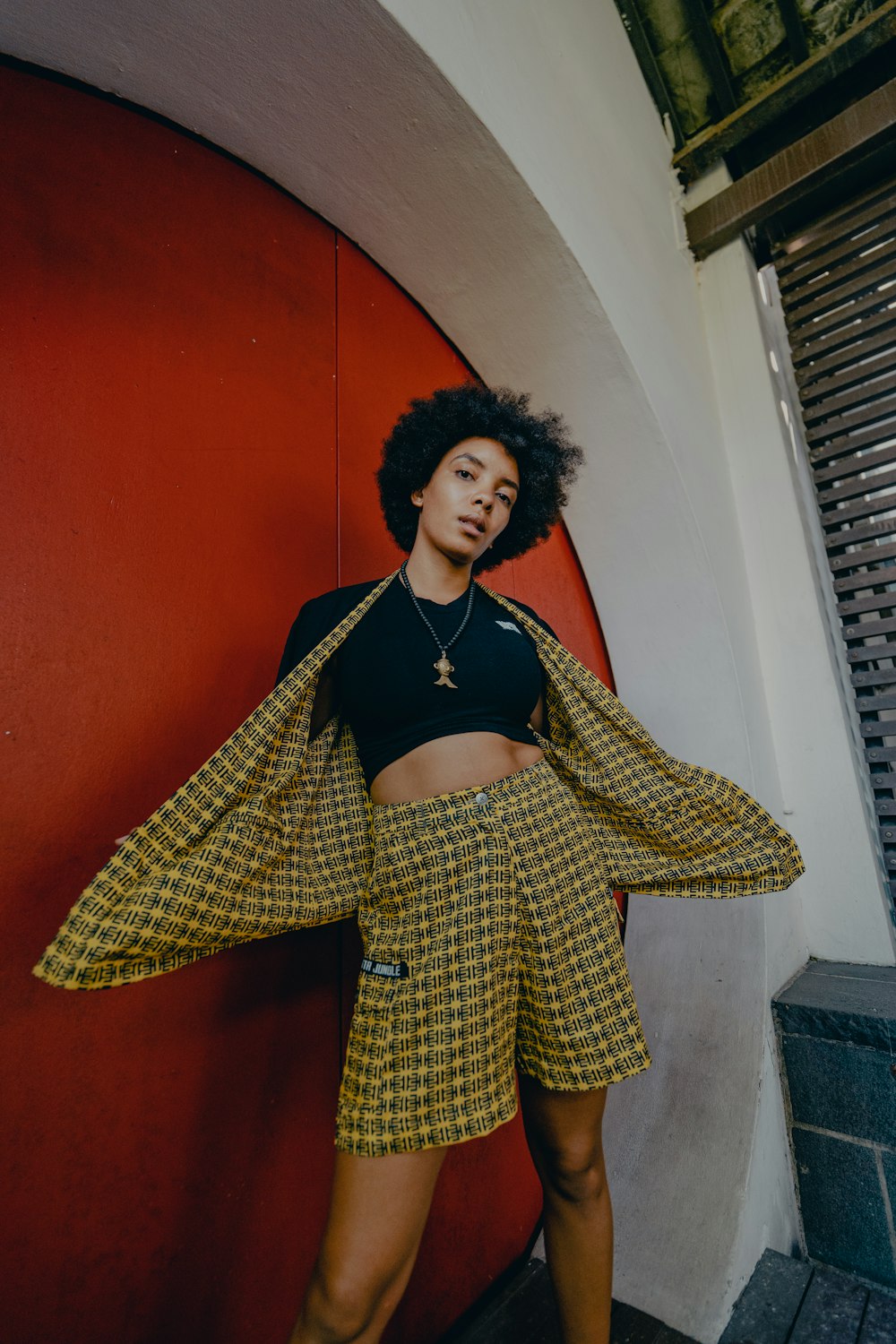 woman in yellow and black checkered coat standing beside red wall