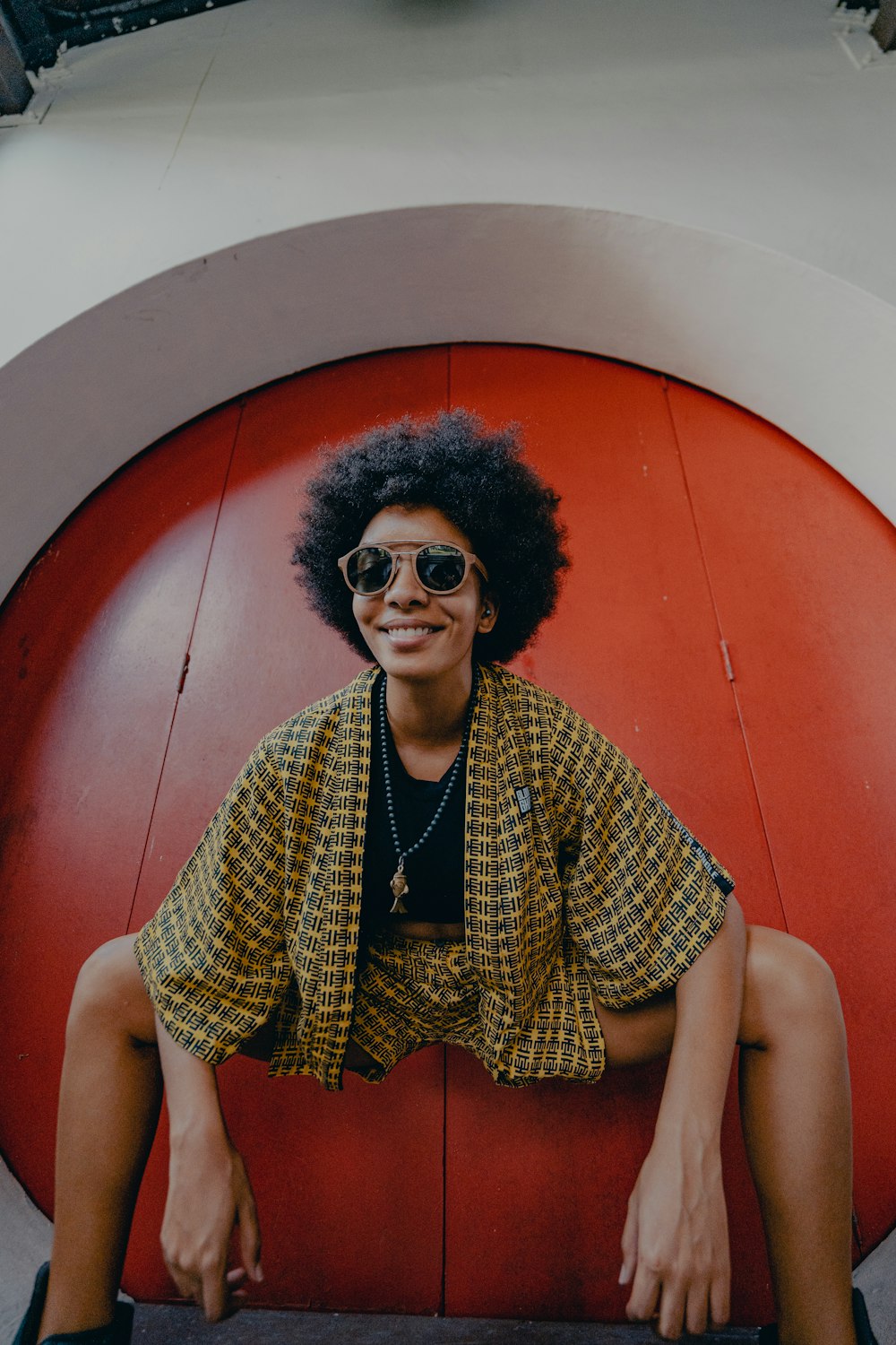 woman in yellow and black polka dot shirt wearing black sunglasses sitting on red chair