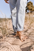 person in blue denim jeans standing on brown sand during daytime