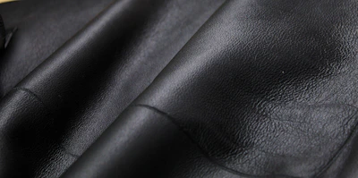 Close-up of premium black leather fabric texture under soft lighting, emphasizing quality craftsmanship.