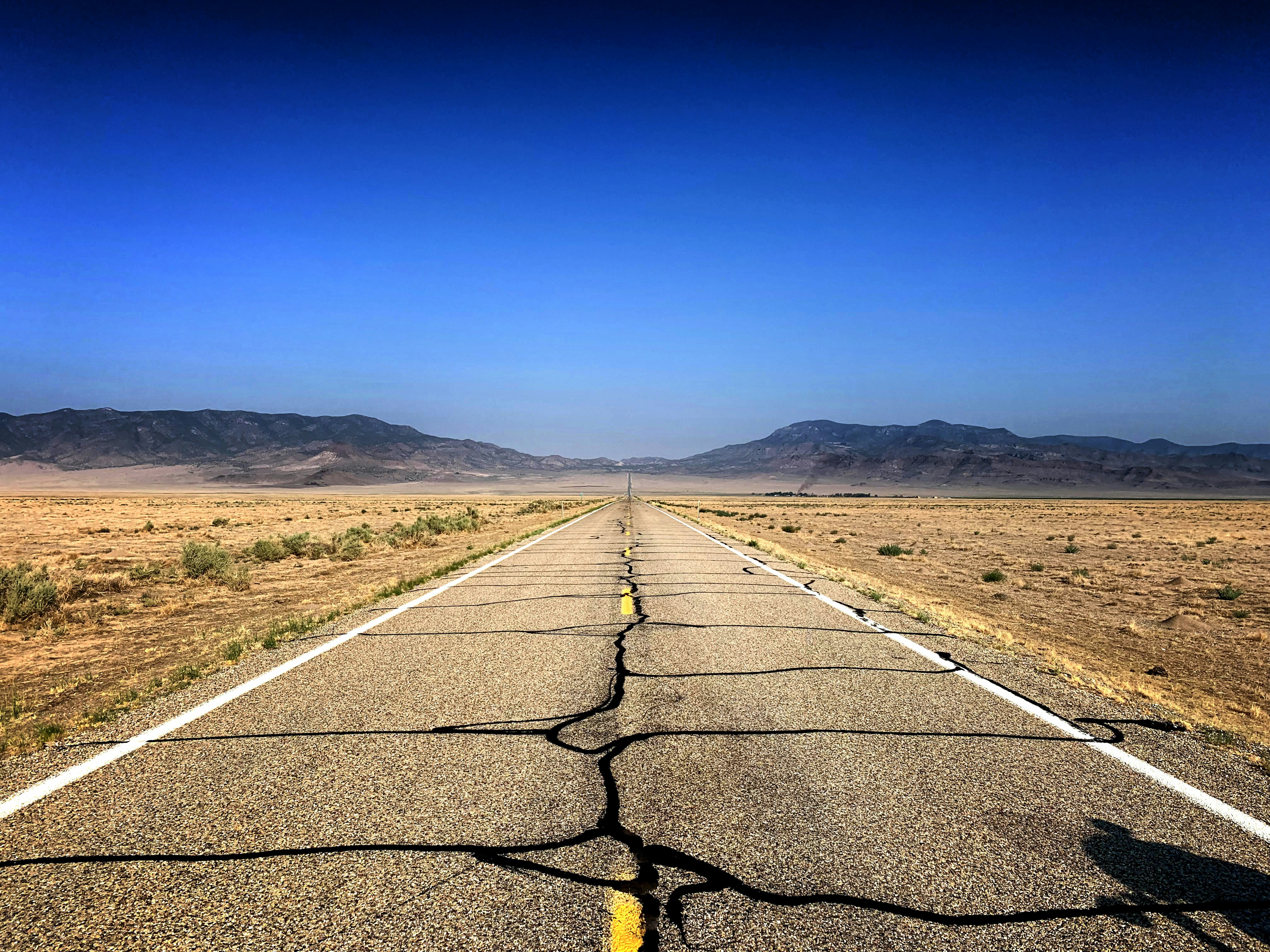 gray concrete road between green grass field under blue sky during daytime, Lonely road in Nevada.