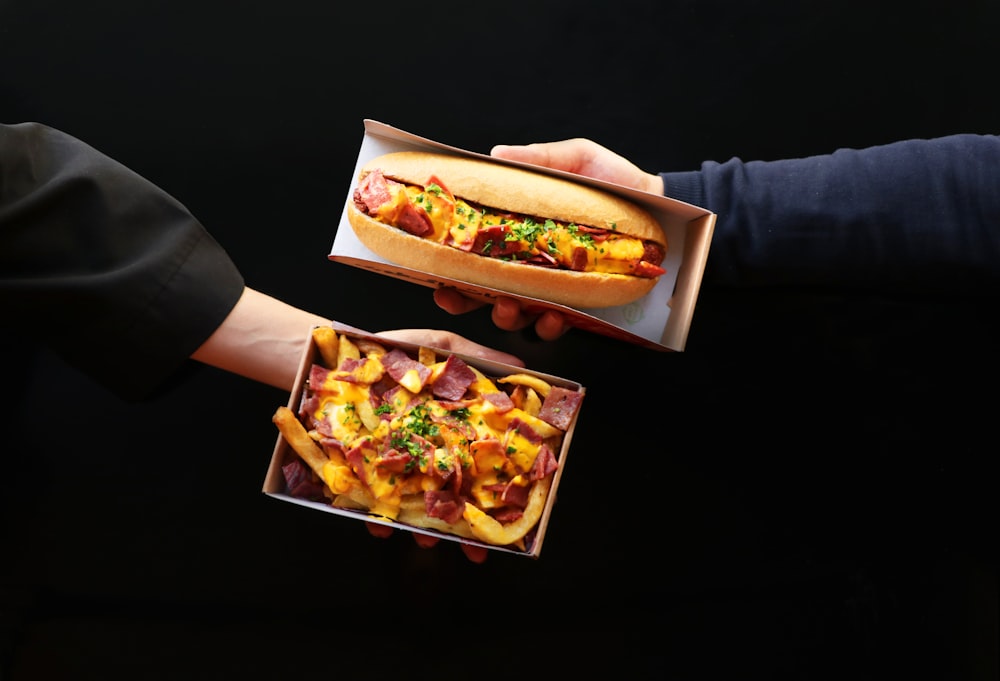 a person holding a hot dog and a box of fries
