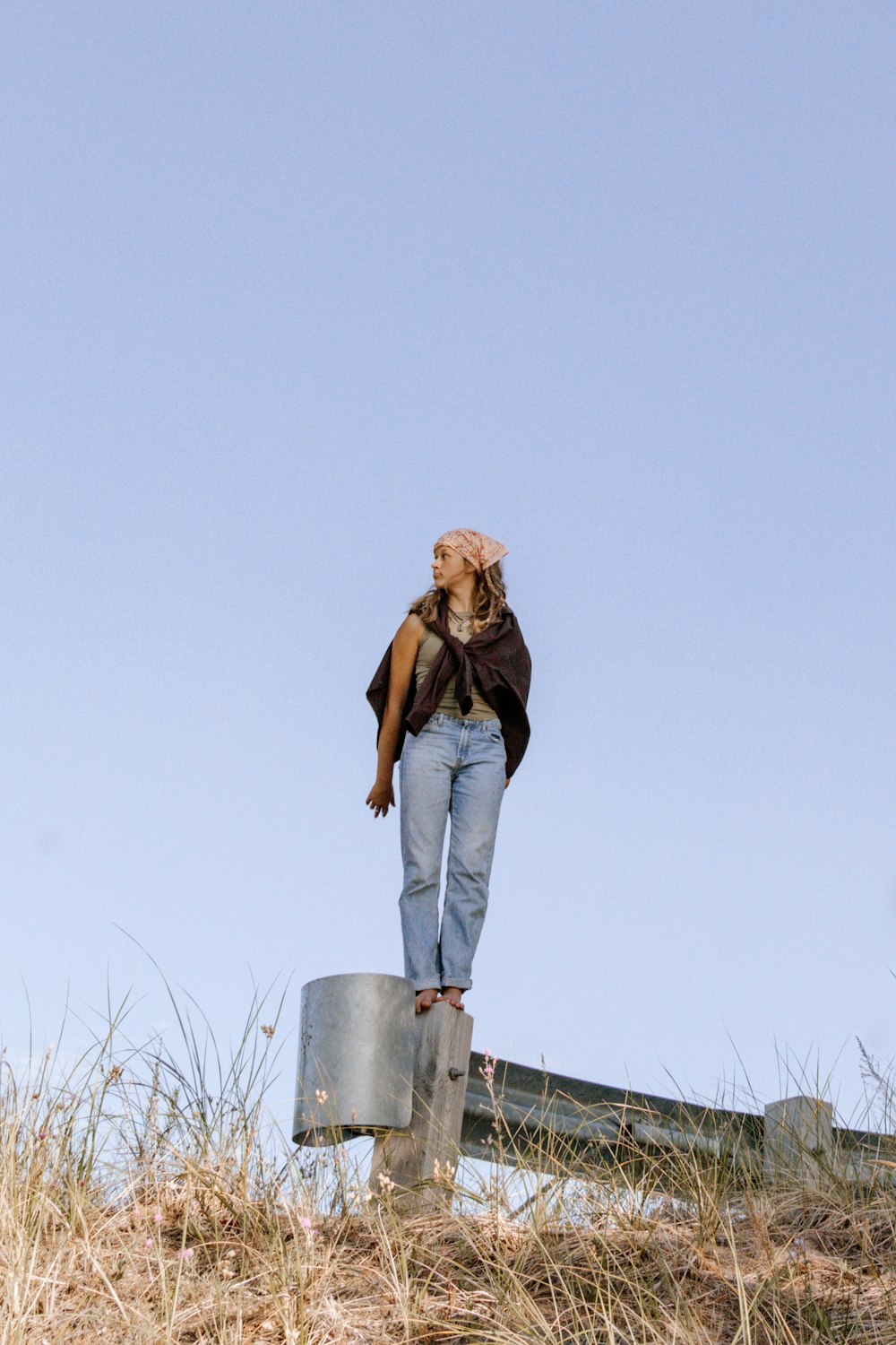 woman in brown knit cap and blue denim jeans standing on wooden fence during daytime