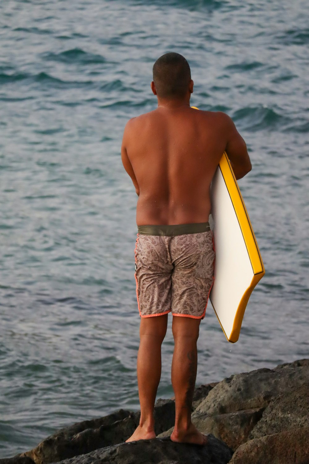 Mann in blau-weißen Shorts mit weißem Surfbrett, der tagsüber am Strand steht