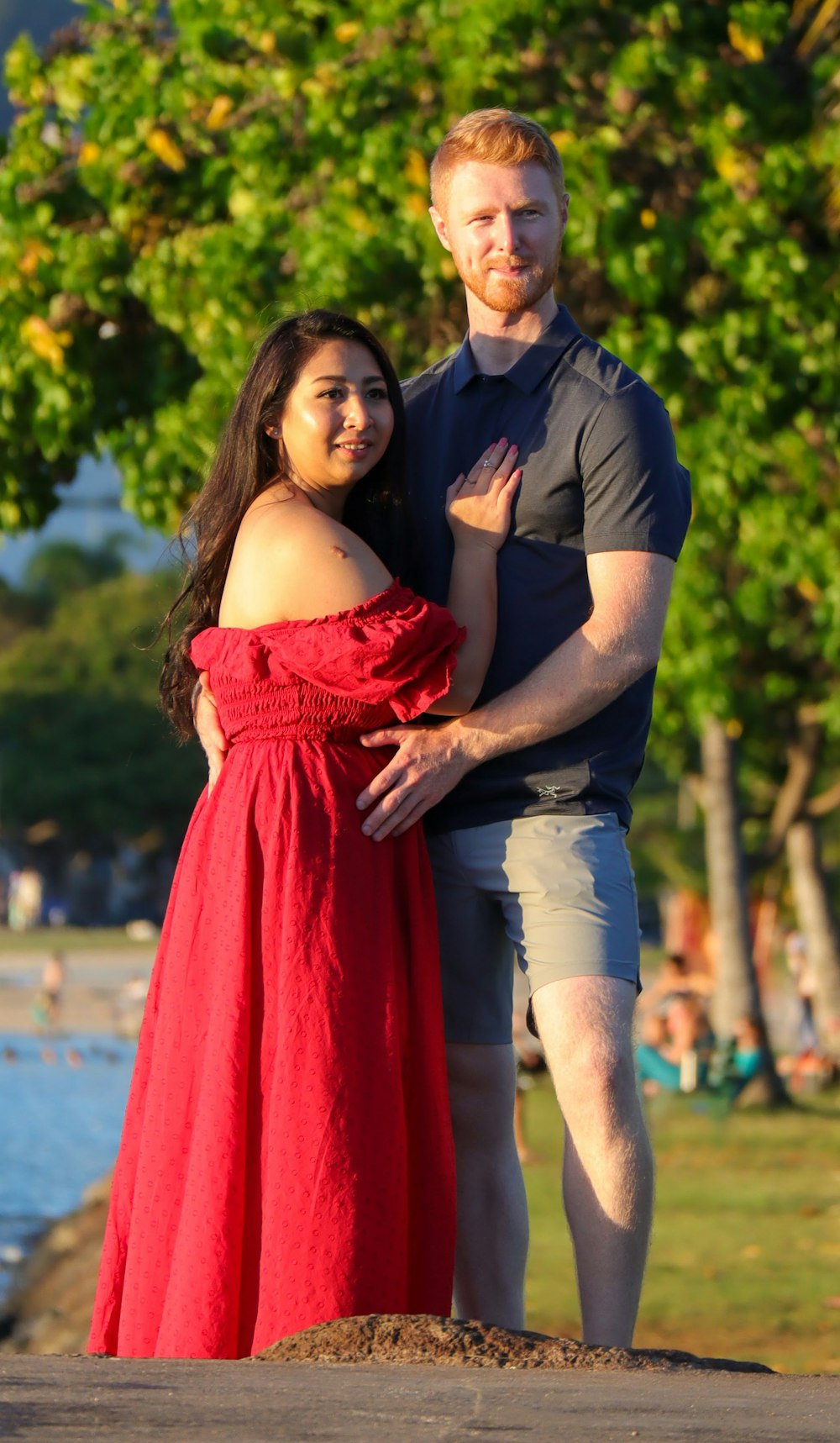 man in black polo shirt hugging woman in red tube dress