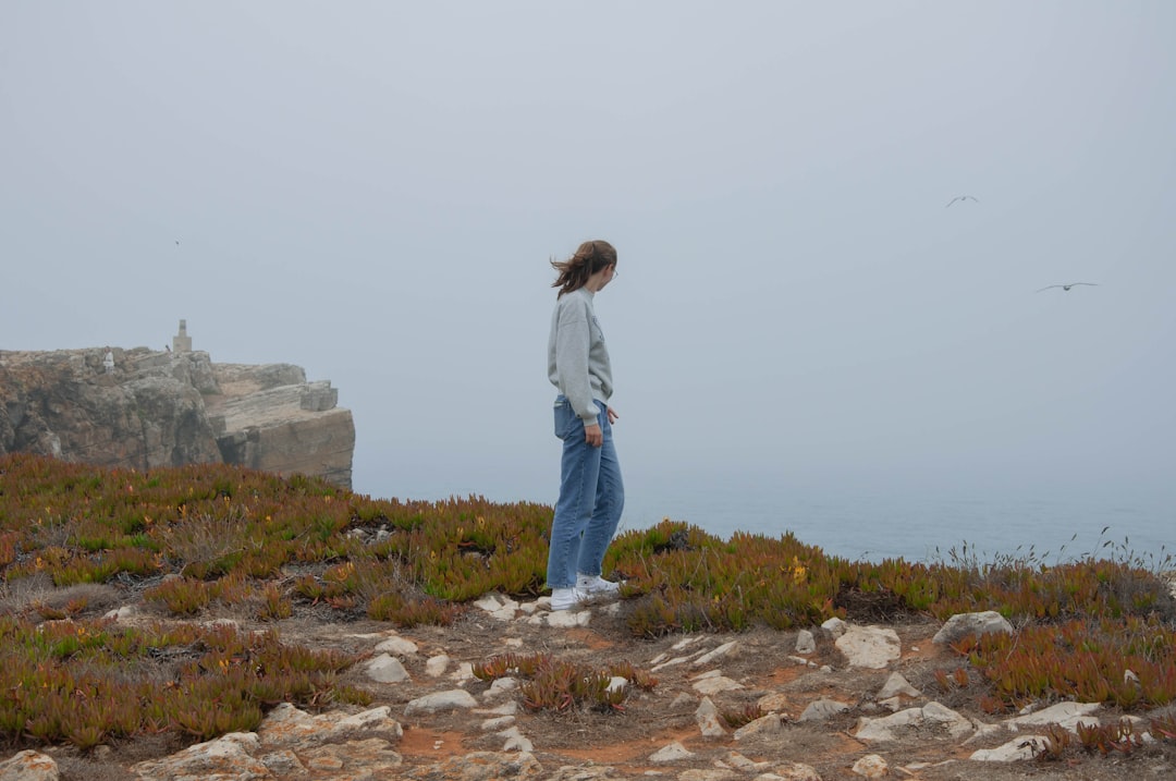woman in white long sleeve shirt and blue denim jeans standing on rocky ground during daytime
