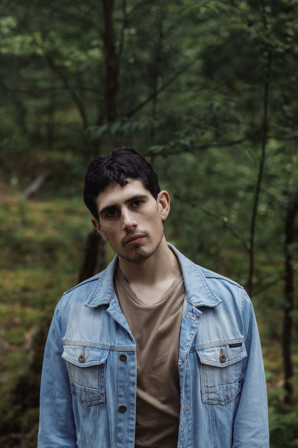 man in blue denim jacket standing near green trees during daytime